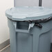A Rubbermaid BRUTE grey trash can with a black lid in a corporate office cafeteria.