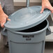 A person opening a Rubbermaid grey trash can lid.