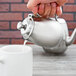 A person pouring cream from a Vollrath stainless steel creamer into a coffee cup.