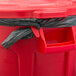 A red Rubbermaid BRUTE trash can with a black bag over it.