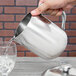 A hand pouring water from a Vollrath stainless steel water pitcher into a glass with ice.