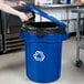 A woman's hand putting a blue Rubbermaid lid on a Rubbermaid blue recycling can.