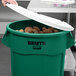 A person putting potatoes in a green Rubbermaid BRUTE trash can with a white lid.