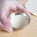 A person in gloves holding a stainless steel hemisphere mold filled with white dough.