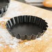 A black metal Matfer Bourgeat fluted quiche mold on a wooden surface.