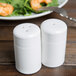 Two Tuxton white china salt shakers on a table with a salad.