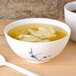 A blue bamboo melamine soup bowl filled with dumplings in soup with a white spoon.