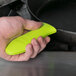 A hand holding a green and yellow Lodge silicone handle holder over a frying pan.