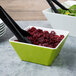 A green and white square melamine bowl filled with salad and dried cranberries.