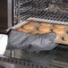 A person in a black Lodge oven mitt taking cookies out of an oven.