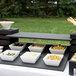 A black wood Vollrath display shelf holding white square bowls of food on a black surface.