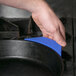 A person's hand holding a blue Lodge silicone handle cover over a black pan.