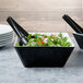 Two black Vollrath melamine bowls filled with salad on a table.