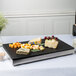 A Vollrath stainless steel cooling plate with cheese and grapes on a table.