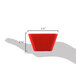 A hand holding a red Vollrath extra-small square melamine bowl.