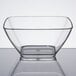 A clear small square Vollrath acrylic bowl on a reflective surface.