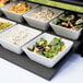 A row of Vollrath white melamine bowls filled with salad.