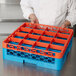 A man holding a blue and orange Carlisle plastic container with a rack of blue and orange trays inside.