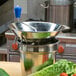 A stainless steel Tellier food mill with a blue handle on top of a metal bowl with vegetables.