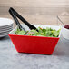 A red Vollrath melamine bowl filled with salad on a table with tongs.