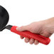 A hand holding a red Lodge silicone handle holder over a black skillet.