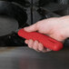 A hand using a red Lodge silicone handle holder on a frying pan.