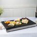 A Vollrath slate and granite melamine tray with cheese and grapes on a table.