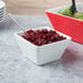 A white small square melamine bowl filled with cranberries with a spoon