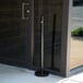 An American Metalcraft black stainless steel free standing smoker pole and base outside of a building with a glass door.