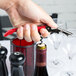 A hand with a red Pulltap's Original Waiter's Corkscrew opening a wine bottle.