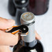 A person using a Pulltap's Original Waiter's Corkscrew with an orange handle to open a bottle of wine.