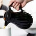 A person pouring coffee into a cup from a black Vollrath SwirlServe coffee pot.