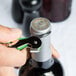 A hand using a Pulltap's Original Waiter's Corkscrew with a lime green handle to open a bottle of wine.