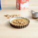 A Gobel fluted non-stick tart/quiche pan with a small pecan pie in it with a small spoon and a small container of cream.