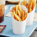 Two white paper cups filled with french fries on a tray.