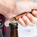 A hand using a Pulltap's Original copper waiter's corkscrew to open a bottle of beer.