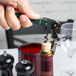 A hand using a Pulltap's Original dark green corkscrew to open a bottle of wine.