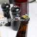 A person using a Franmara Tavern Wing Corkscrew with a white body to open a beer bottle on a counter.