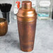 An American Metalcraft satin antique copper cocktail shaker on a counter.