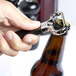 A hand using a Franmara chrome-plated cork extractor with a black sheath to open a bottle of beer.