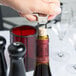 A person using a Franmara Ahh Super! Chrome-Plated Cork Extractor with a black sheath to open a bottle of wine.