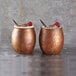 Two American Metalcraft satin antique copper Moscow mule tumblers on a table with a spoon and raspberries.
