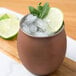 An American Metalcraft antique copper Moscow Mule tumbler filled with ice and lime wedges.