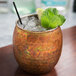 An American Metalcraft hammered antique copper Moscow Mule tumbler filled with ice and mint leaves.