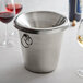 A Franmara stainless steel spittoon on a counter next to wine glasses and a bottle of red wine.
