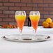 A Vollrath stainless steel serving tray with glasses of yellow and orange liquid on it.