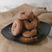 A GET black matte square melamine plate with a pile of donuts on it.