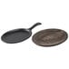 A Lodge pre-seasoned cast iron fajita skillet with a wooden underliner on a table.