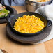 A Lodge mini cast iron round casserole dish filled with macaroni and cheese on a table with a bowl of chips.