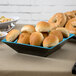 A table with a blue and black square melamine bowl filled with bagels.